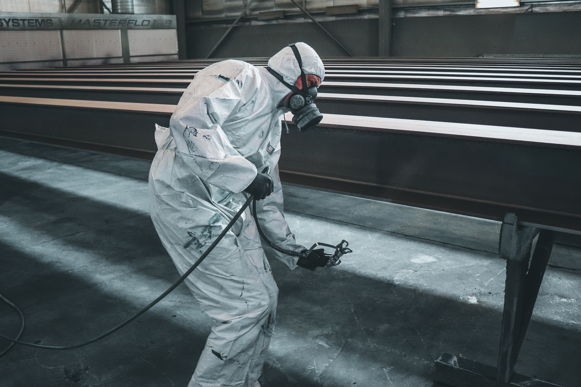 A worker in protective gear spray-applying a specialty coating to metal — commercial industrial painting services