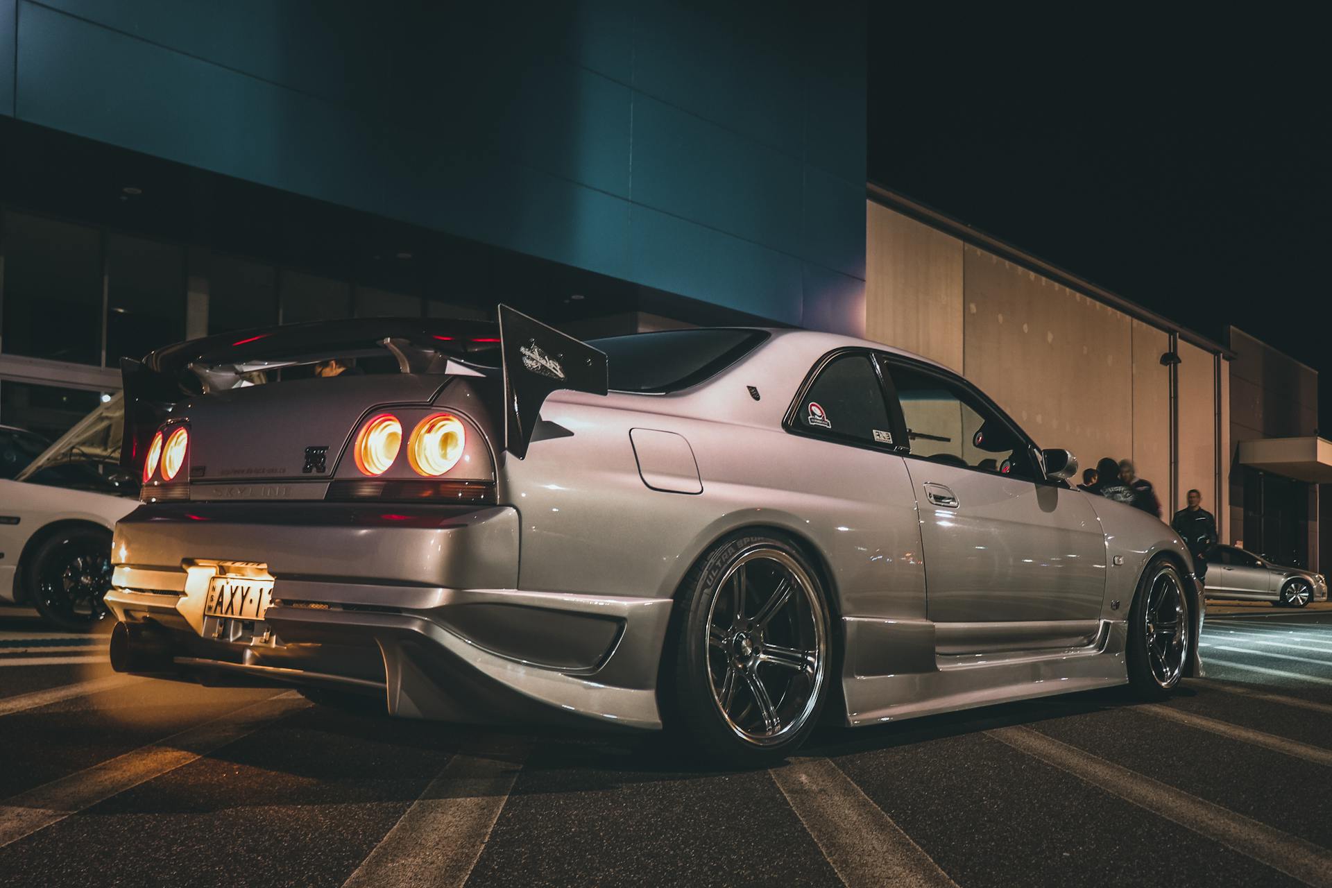 A silver sports car with a prominent spoiler parked at night in an urban setting.