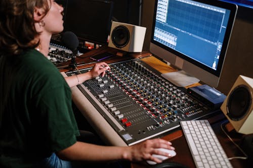A Person in Green Crew Neck T-shirt Sitting Infront of Computer and Audio Mixer