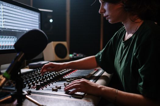Focused woman operates a sound mixer in a music studio, enhancing audio quality.