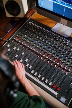 Top view of a person adjusting a large audio mixer in a studio setup with computer monitor and speaker.
