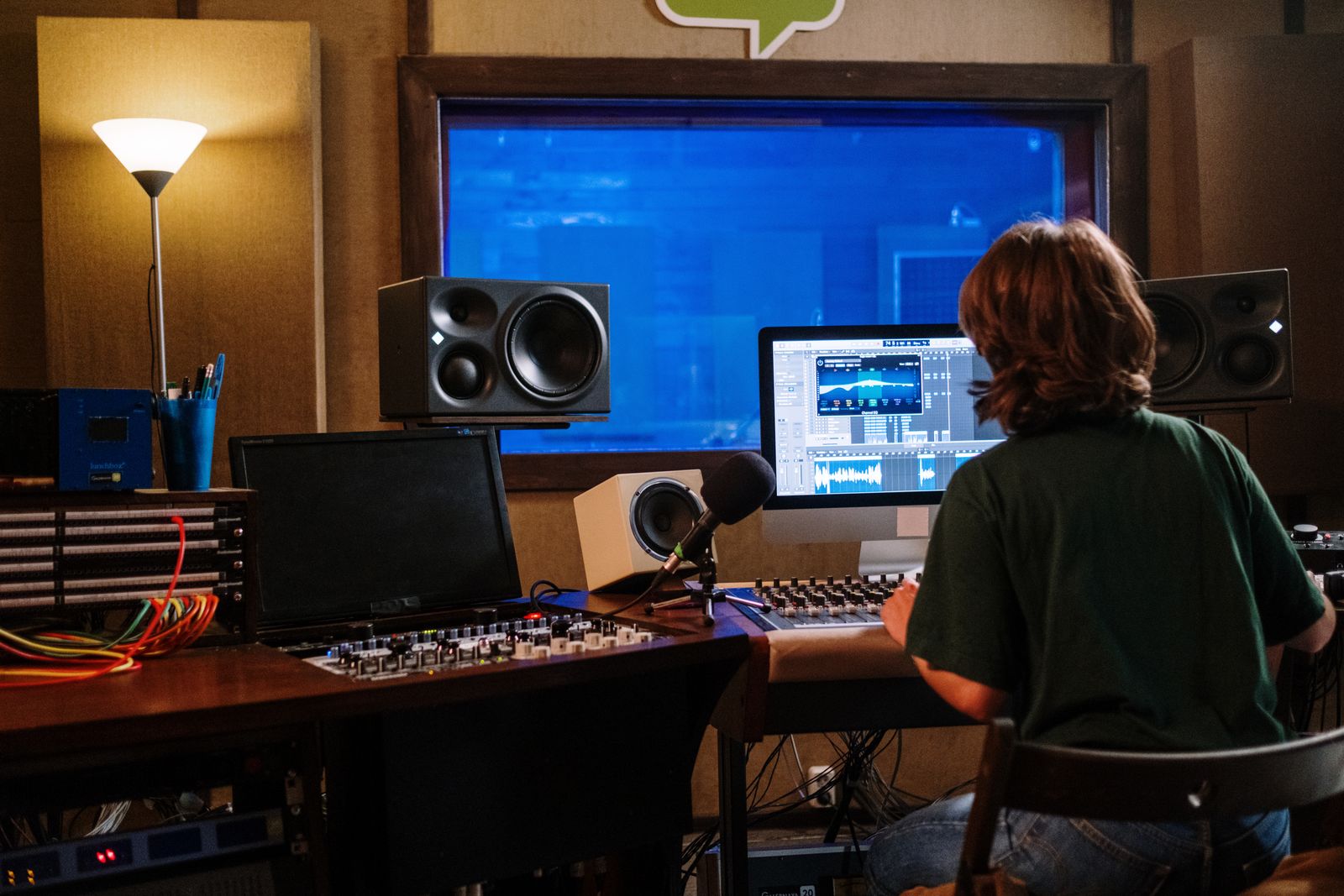 Audio engineer at a studio desk facing monitors and speakers.