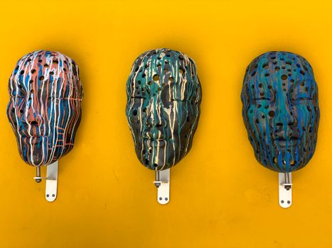 Three artistic masks with paint drips mounted on a vibrant yellow wall.