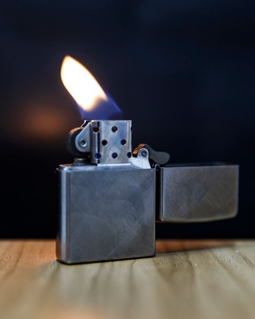 Free Close-up of a silver flame lighter on a wooden surface against a dark background. Stock Photo