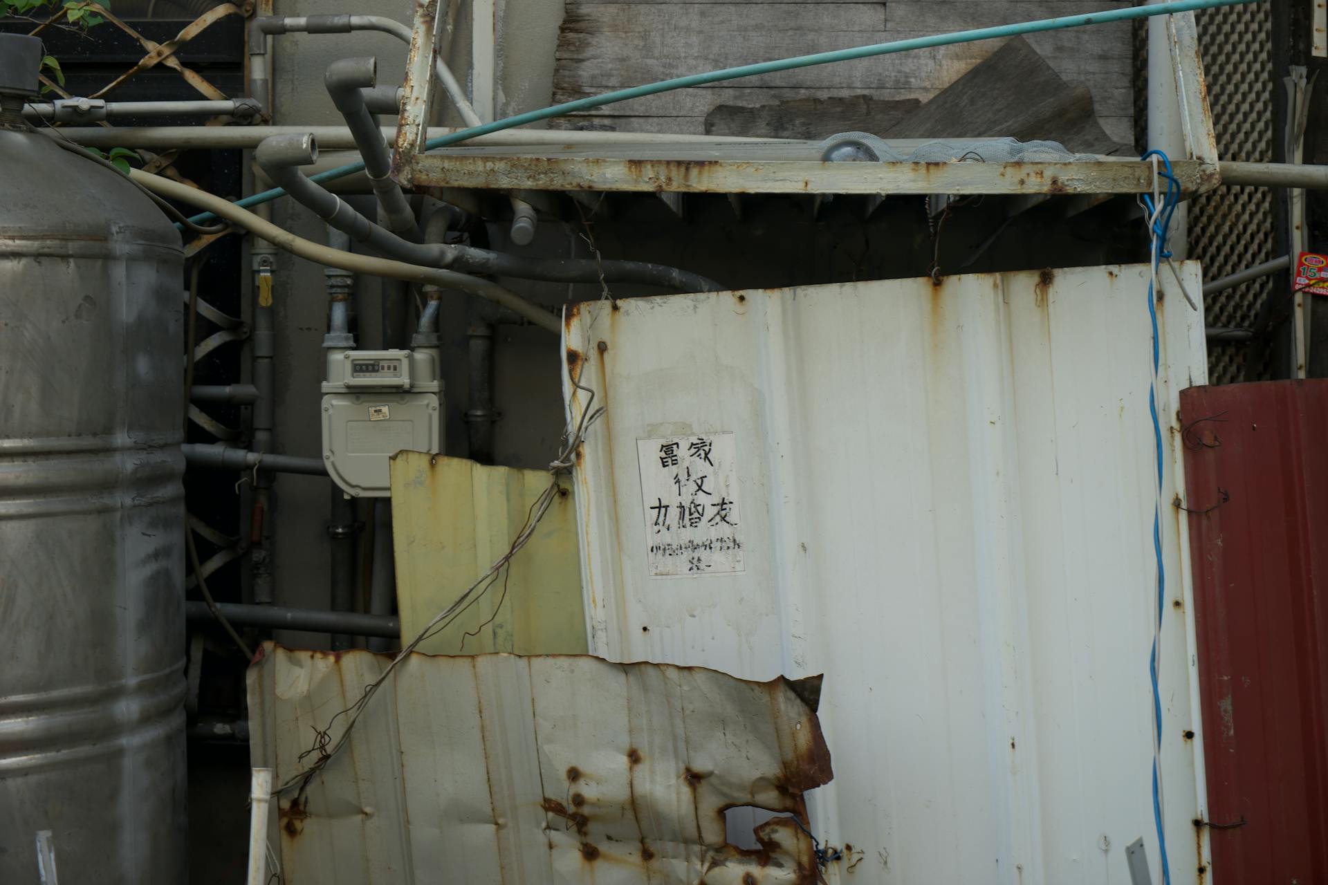 Close-up of rusty metal panels and exposed industrial pipes in an urban area.