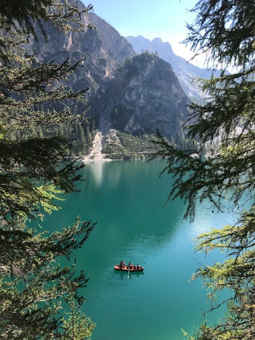 People Riding a Wooden Boat on Green Lake Near Mountains