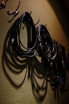 Coiled black cables hanging on hooks casting shadows on a textured wall.