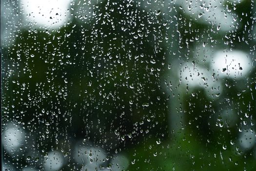 雨滴清晰地落在玻璃窗上，背景是模糊的绿色自然景色