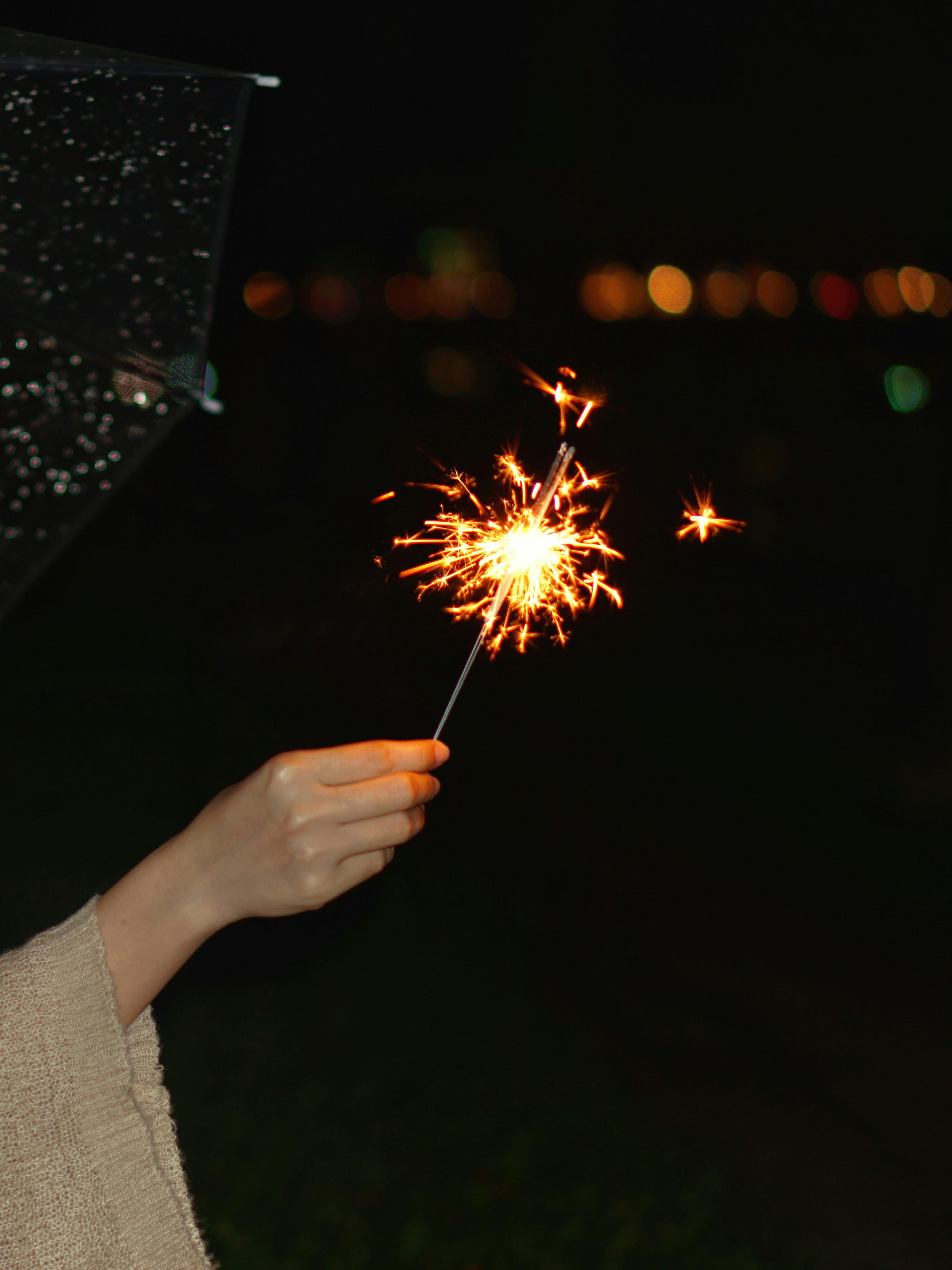 Crop unrecognizable female showing bright Bengal light with sparks illuminating street at dusk
