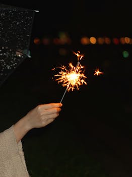 Crop unrecognizable female showing bright Bengal light with sparks illuminating street at dusk