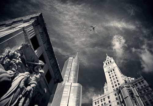Gri Tonlamalı Fotoğrafçılıkta Beton Binalar Ve Heykeller üzerinde Uçan Hava Uçağı