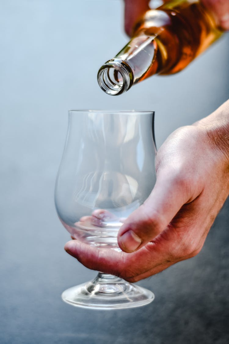 A Hand Pouring Brown Liquid On A Glass