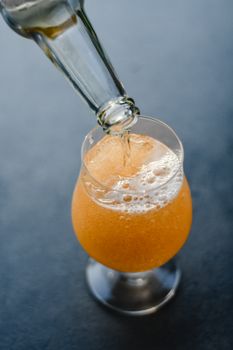 特写：将明亮的橙色碳酸饮料倒入深色背景的玻璃杯中