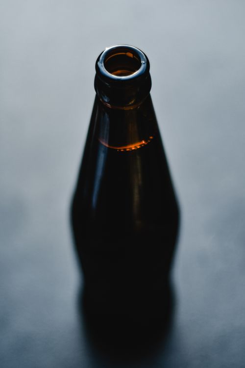 Free A dark beer bottle captured from above, showcasing its shiny surface and reflective qualities on a blue background. Stock Photo
