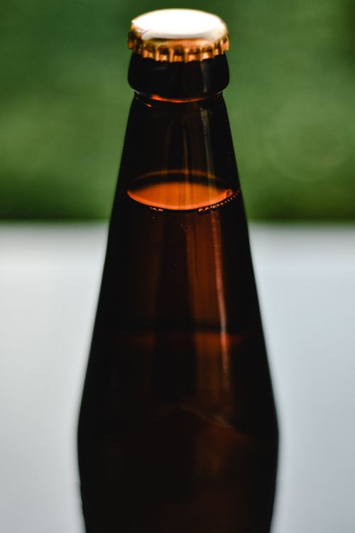 Free Detailed shot of an amber beer bottle with cap, shot against a blurred green backdrop. Stock Photo