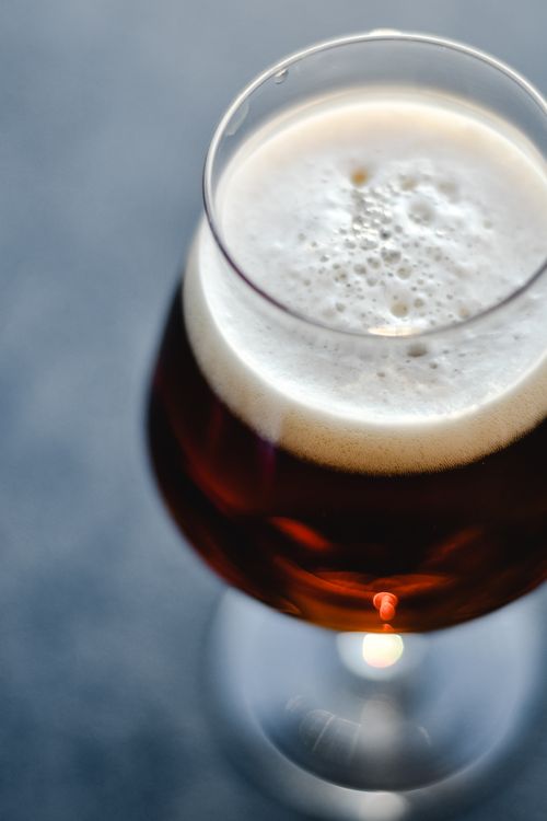 Free High angle view of a glass filled with frothy beer, showcasing the foam head and rich amber color. Stock Photo