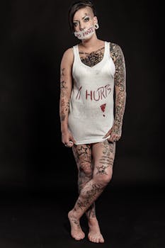 Portrait of a tattooed woman in a tank top with message 'It Hurts', on a black background.
