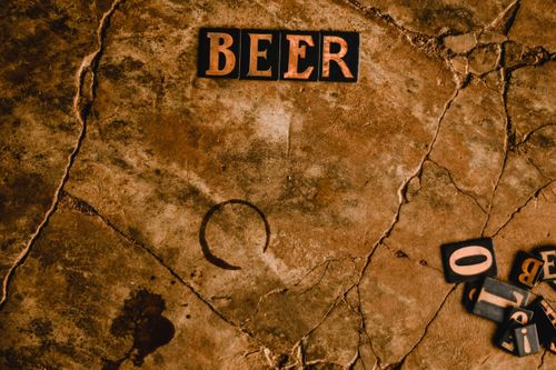 Free Letter tiles spelling 'BEER' on a rustic, cracked surface with scattered letters. Stock Photo