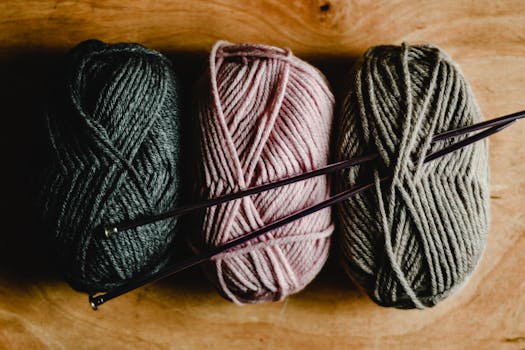 Three yarn balls with knitting needles placed on a wooden surface, ideal for crafting projects.