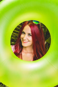 红发女人快乐地透过充气戒指凝视着，笑容灿烂