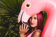 红发女子在户外与粉色充气火烈鸟在热带树叶前合影