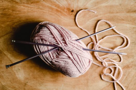 A pink yarn ball with silver knitting needles on a wooden surface, perfect for crafting and knitting projects.