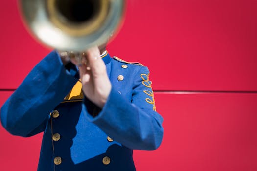 Artist in blue uniform playing trumpet against vibrant red background. Captures music and movement.