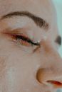 Closeup of anonymous female with plucked eyebrows and closed eyes with mascara on long eyelashes with smudged makeup on face