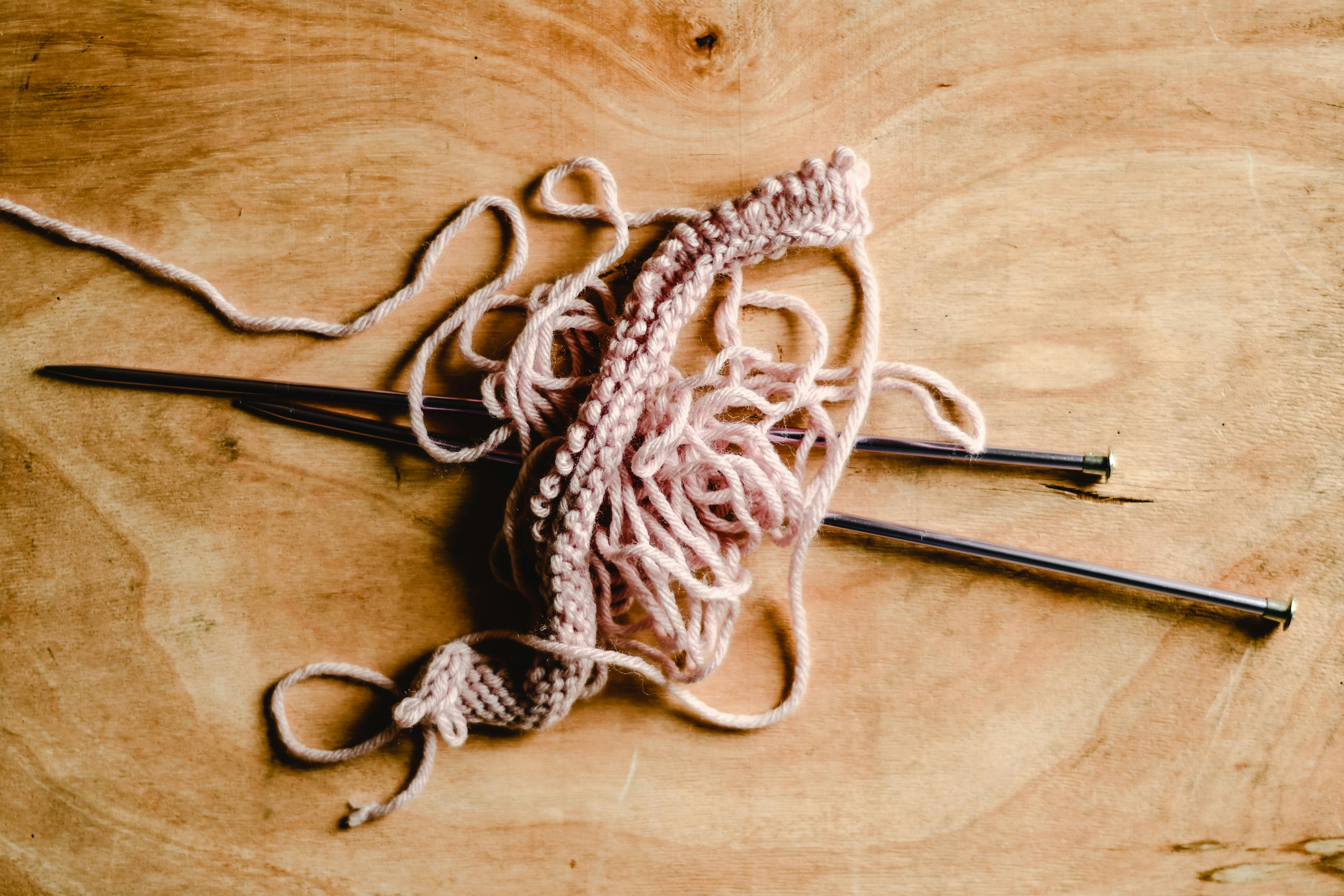 A close-up view of pink yarn and knitting needles on a wooden table, ideal for crafts and DIY themes.