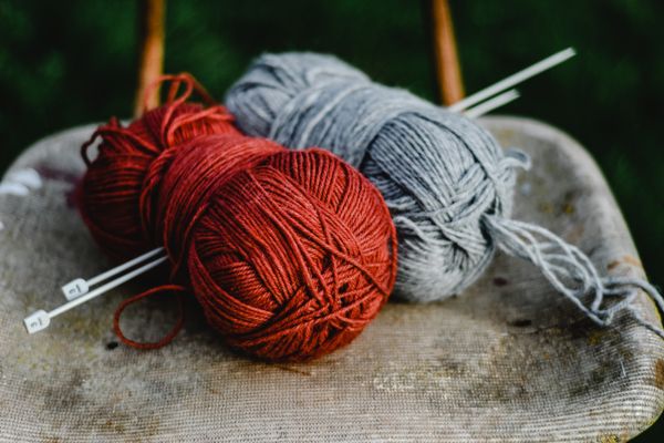 Red and grey yarn balls with knitting needles on a rustic chair — Eva Bronzini on Pexels
