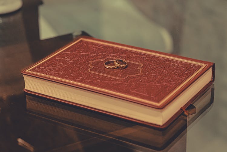 Wedding Rings Placed On Red Book On Glass Table