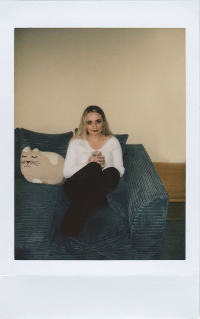 A woman sitting relaxed on a couch with a cat pillow, looking at the camera.