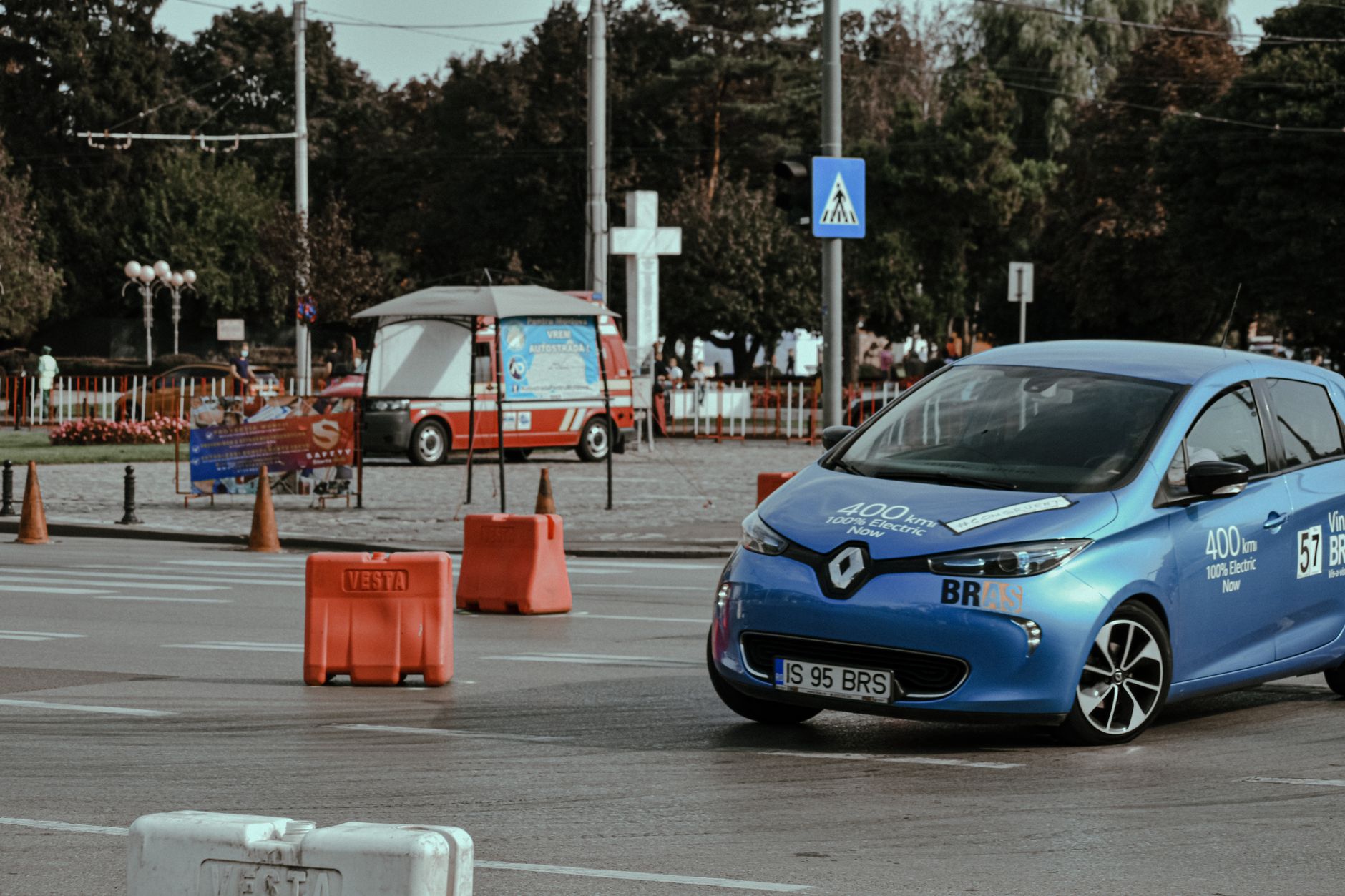 Blue electric car navigating through a city street marked by traffic cones.