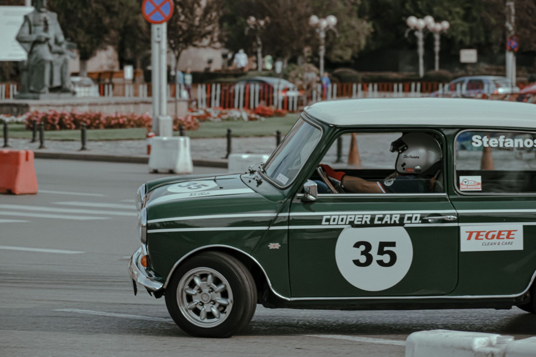 Small green vintage car with driver in helmet on asphalt street during rally