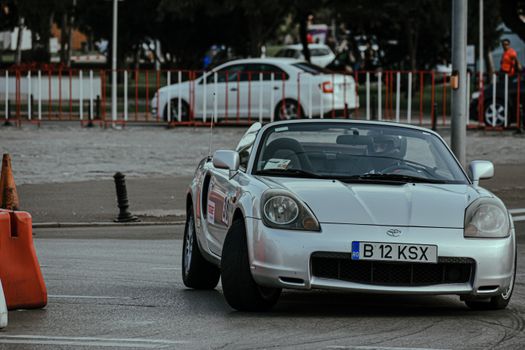 Silver cabriolet car racing in urban rally and driving on asphalt roadway in city