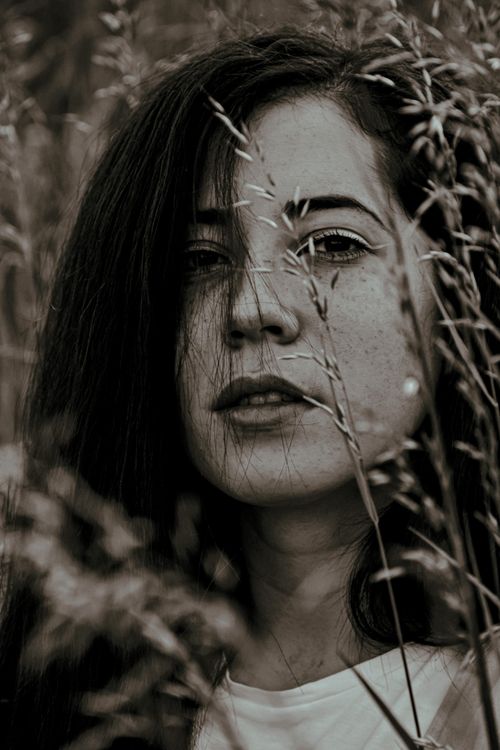 Free Thoughtful female with dark hair looking at camera while standing near tall grass while resting in nature on summer day Stock Photo