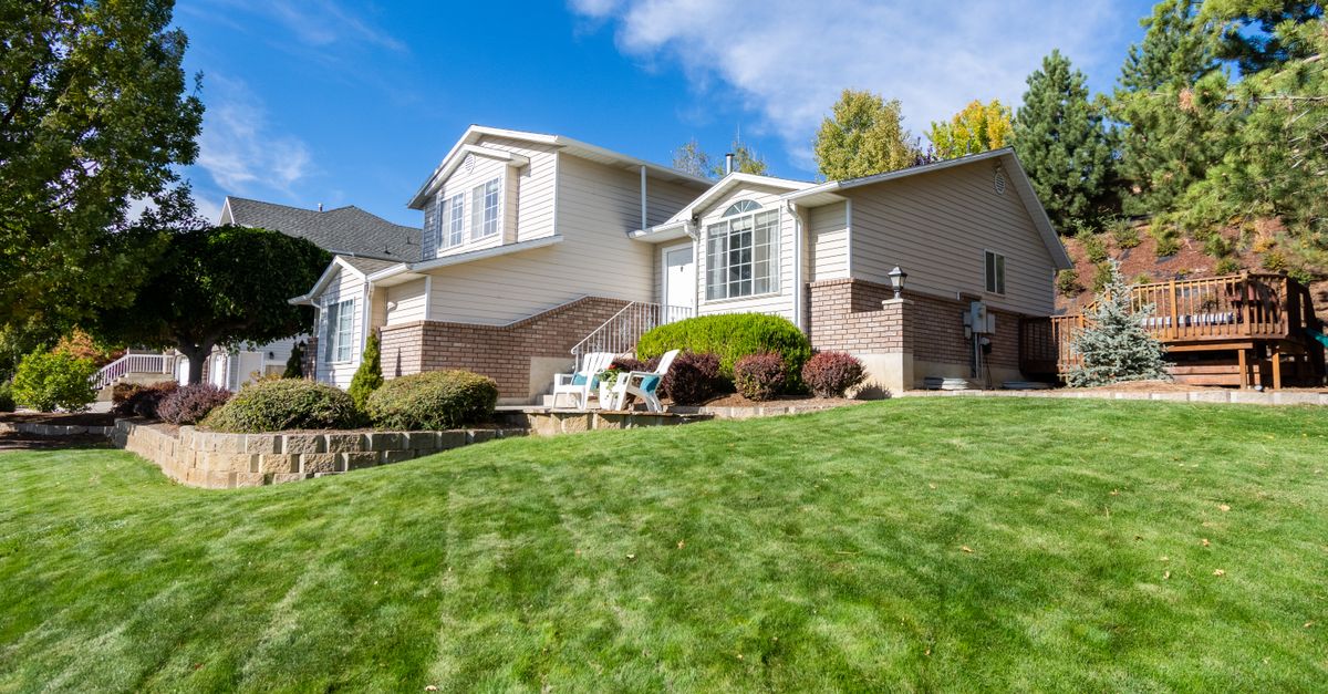 Beautiful suburban house with a manicured lawn, framed by trees and blue sky.