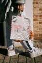 Crop faceless female in trendy outfit holding shopping bag with magazine while strolling on pavement