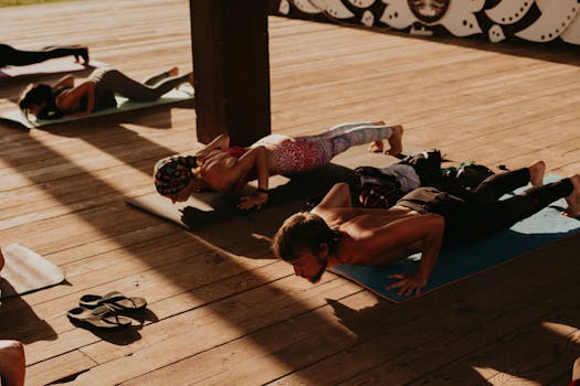 Group of adults doing yoga outdoors on wooden floor in natural light.