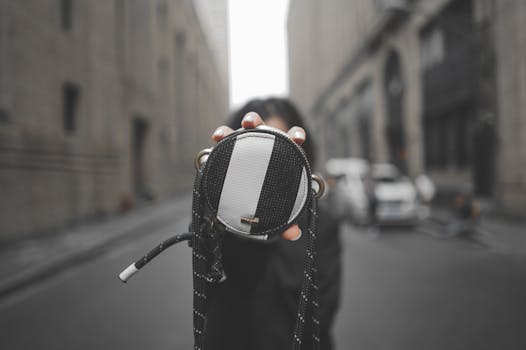 Close-up view of a fashionable round bag held out on an urban street setting.