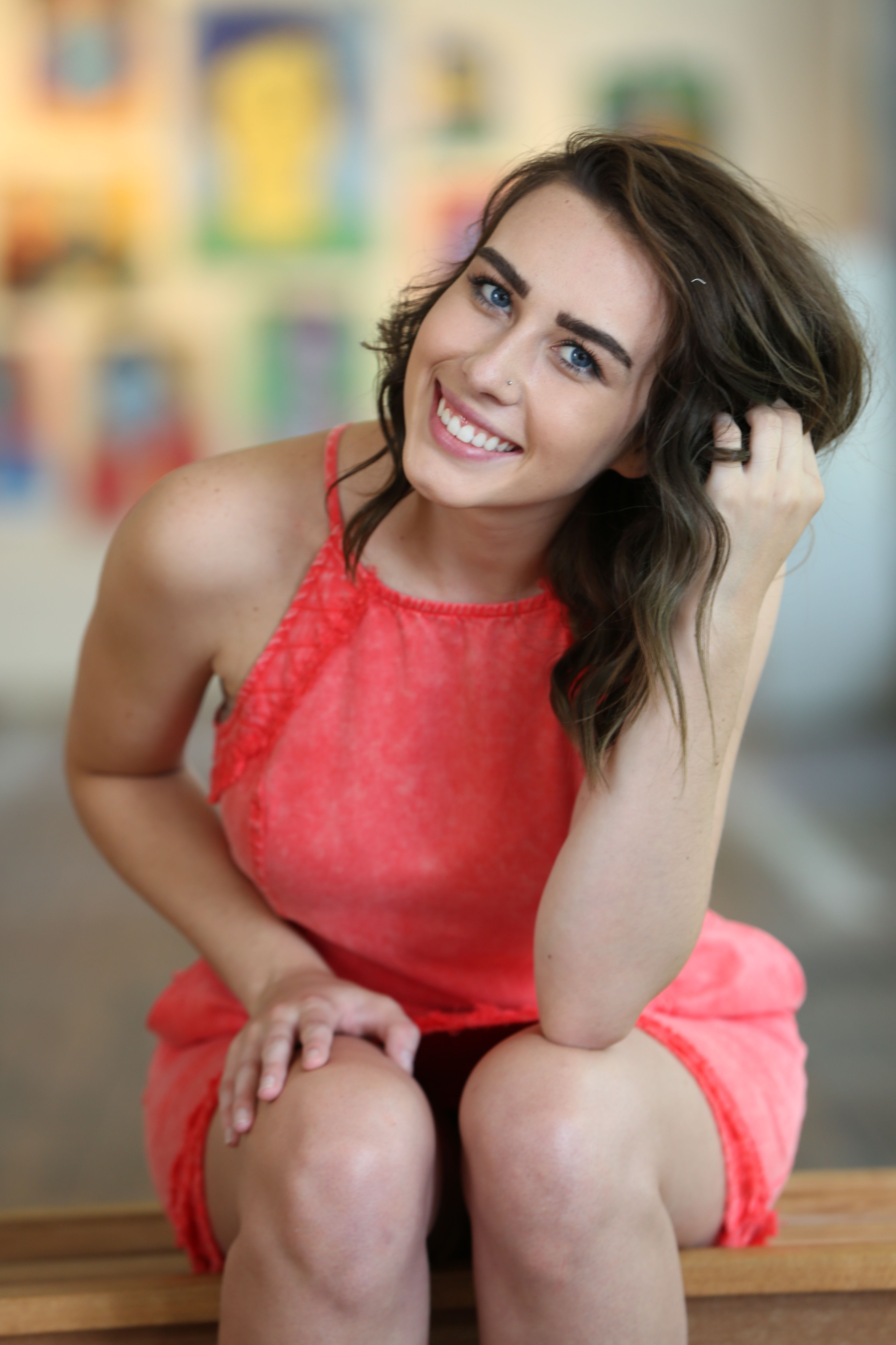 Portrait of a cheerful woman in a sleeveless coral dress sitting indoors, smiling warmly.