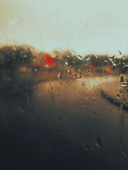 Artistic focus on raindrops on a window with blurred scenery at dusk, creating a moody atmosphere.