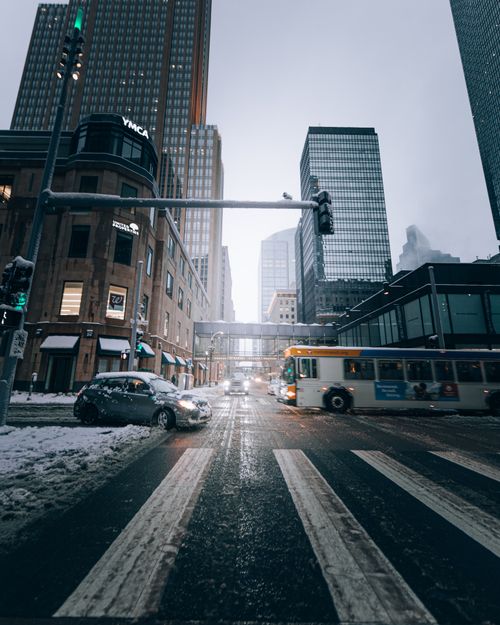 Free Urban winter scene with snow, vehicles, and tall buildings at a city intersection. Stock Photo