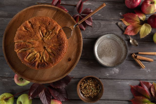 A homemade apple cake surrounded by autumn leaves and spices, top view.