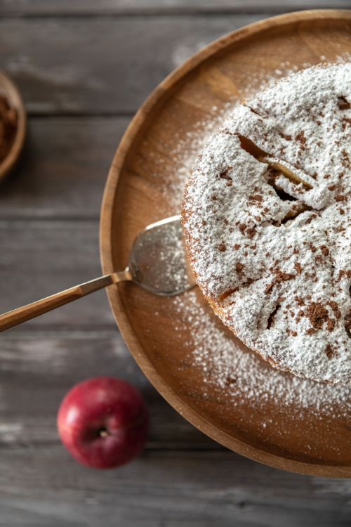 Free Delicious apple cake dusted with powdered sugar on a wooden plate. Perfect for dessert lovers. Stock Photo