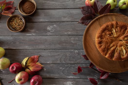 Top view of a rustic apple cake with spices and leaves on a wooden table.