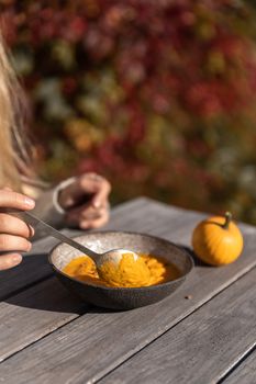 Warm pumpkin soup served outdoors on a rustic table in autumn sunlight.