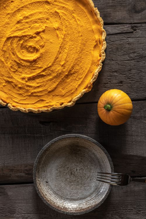 Free Top-down view of a homemade pumpkin pie next to a small pumpkin and empty bowl on a rustic wooden table. Stock Photo