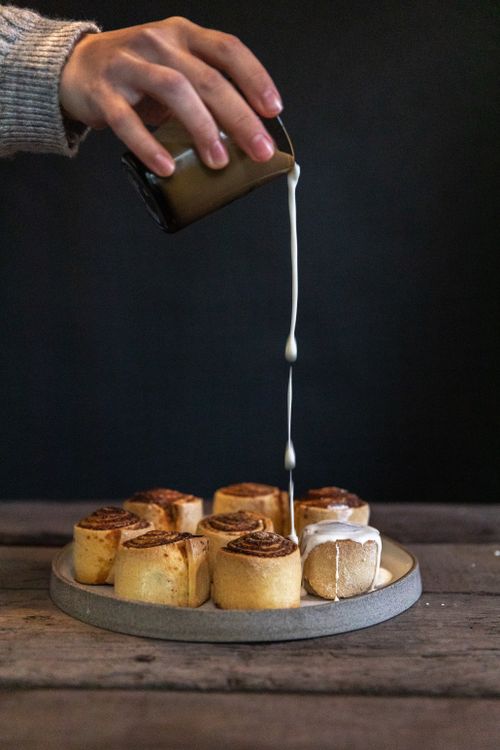 Free Close-up of cinnamon rolls being drizzled with cream, capturing indulgence and texture. Stock Photo