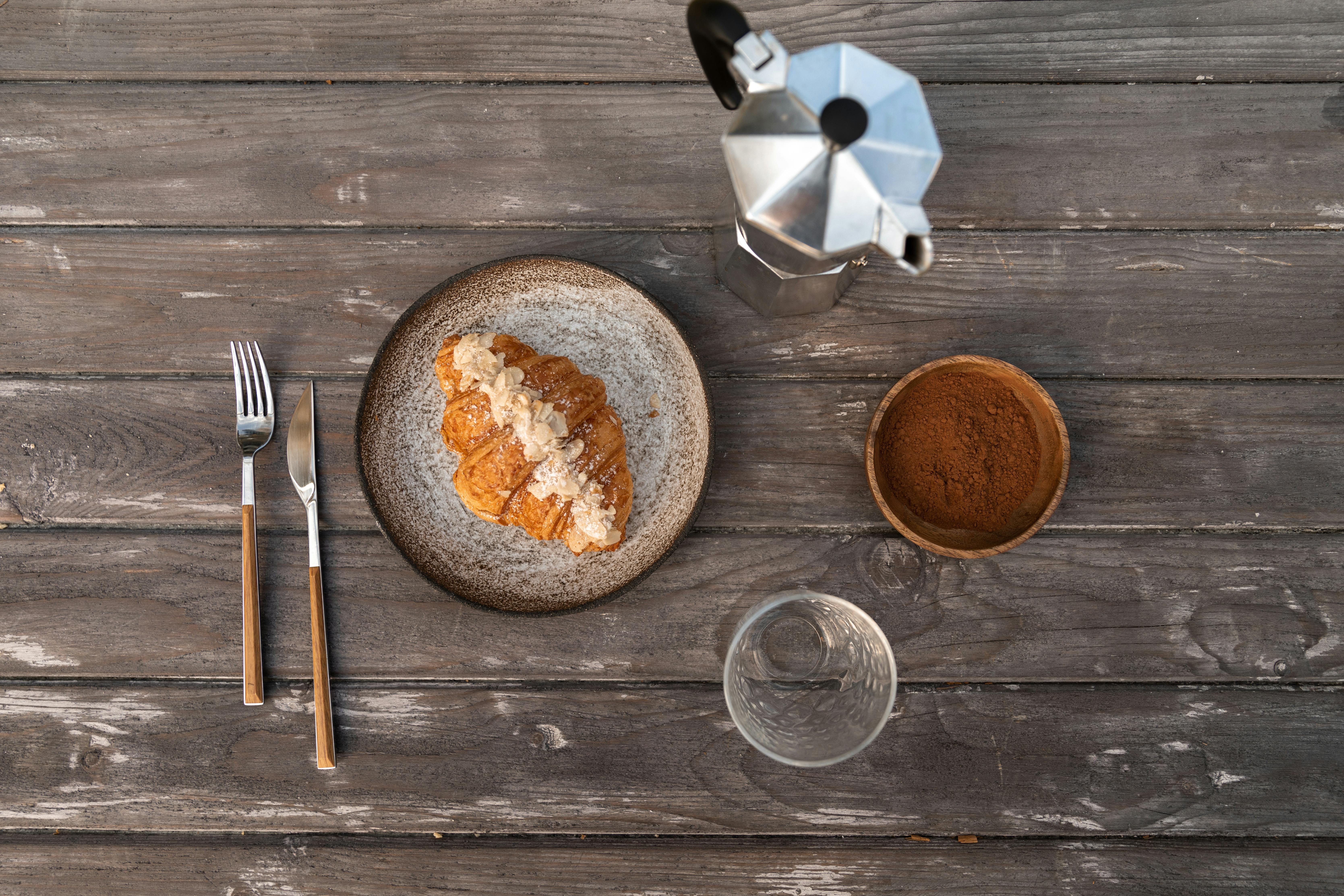 a croissant on a plate beside a moka pot